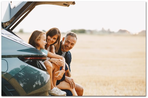 Familie med mor, far og stor pige sidder i bagagerum af bil